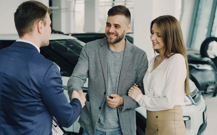 Couple concluant l’achat d’une voiture avec un vendeur en concession